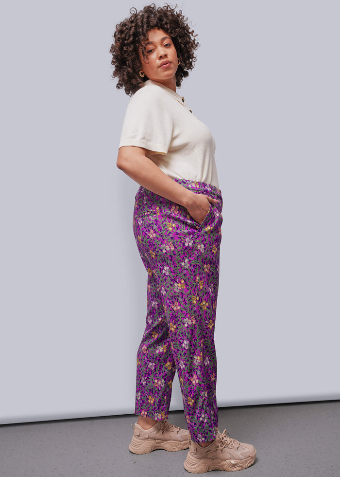 1X=Person wearing a white shirt and purple floral pants against a plain background