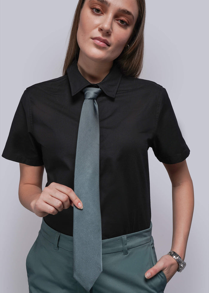 Woman wearing a black shirt with a long light blue tie against a plain background