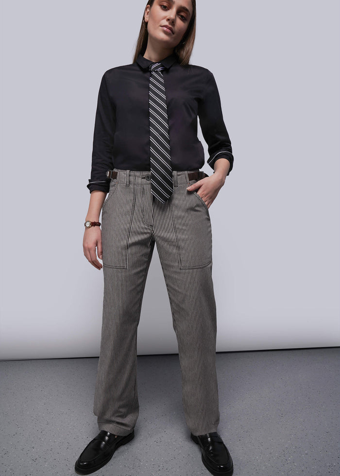 Person wearing a black shirt, striped tie, and gray pants against a plain background