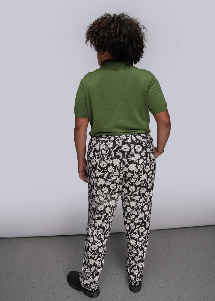 1X=Person wearing a green polo shirt and black and white floral pants against a plain background