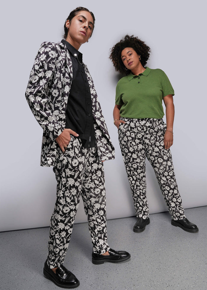 Two people wearing matching black and white floral suits against a plain background