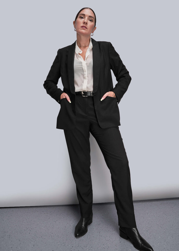 S=Person wearing a black suit with a white shirt on a gray background