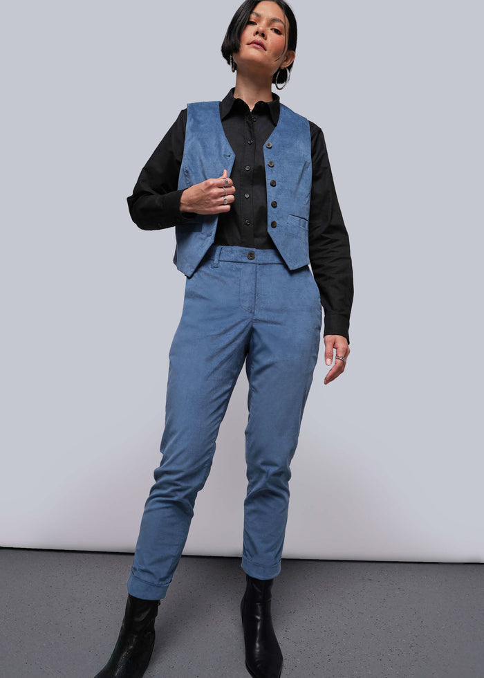 S=Person wearing a blue vest and pants with a black shirt against a plain background