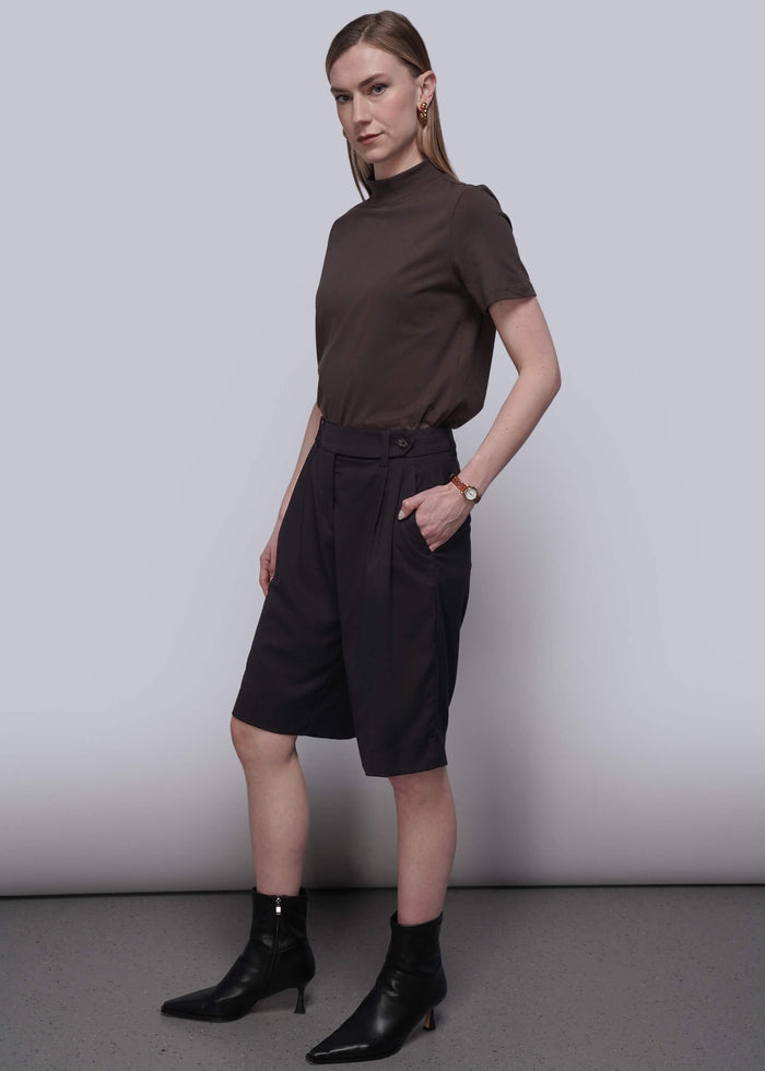 S=Woman wearing a brown top and black shorts with black boots against a plain background