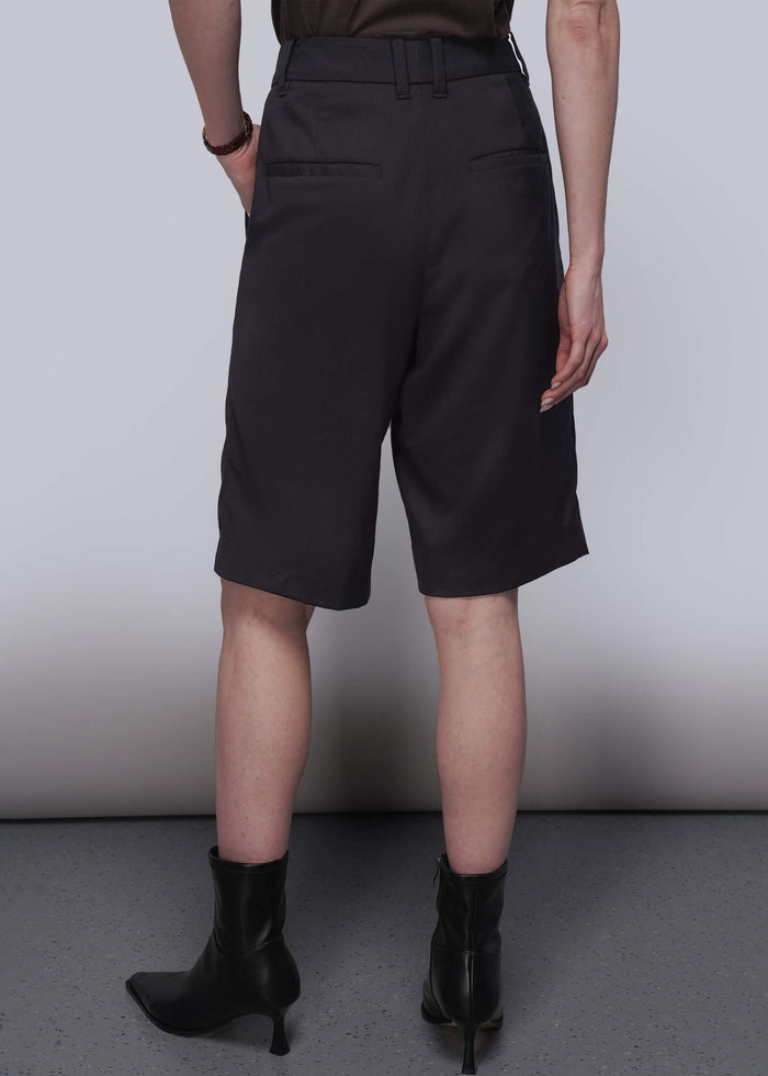 S=Pictured from the back, a person wearing black shorts and black boots against a plain background