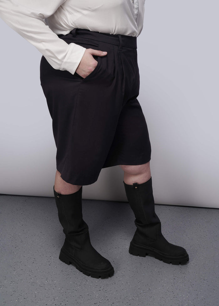 1X=Person wearing black shorts and black boots against a plain background
