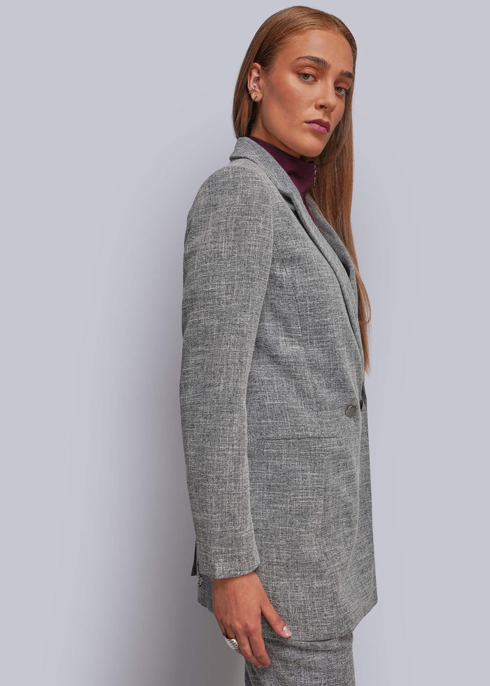 S=A woman wearing a tailored gray blazer with a subtle textured pattern, styled over a dark plum turtleneck, shown in a side-profile studio shot against a light gray background.