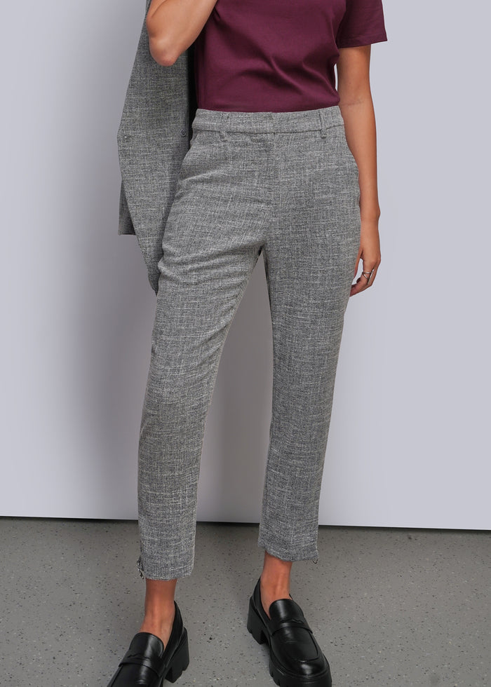 S=A model wearing a pair of gray textured cropped trousers, styled with a dark burgundy t-shirt, a draped gray blazer, and black leather loafers against a light gray studio background.