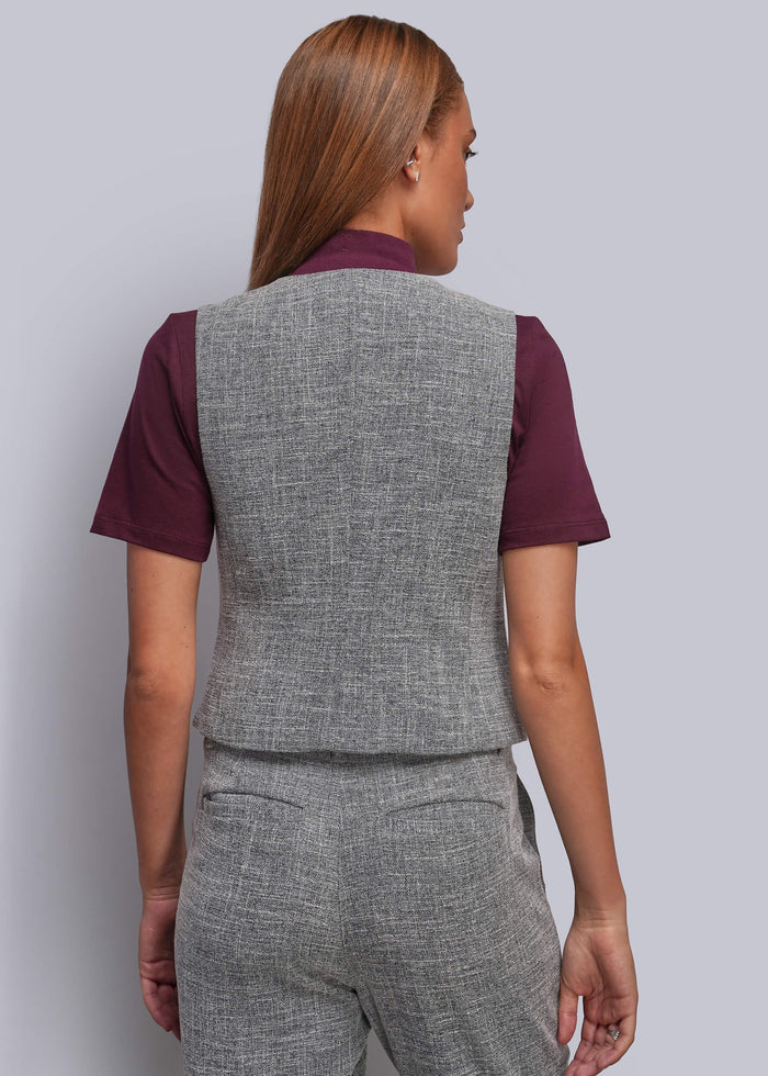S=A woman shown from the back wearing a gray textured vest over a burgundy short-sleeve shirt and matching gray trousers, against a light gray studio background.