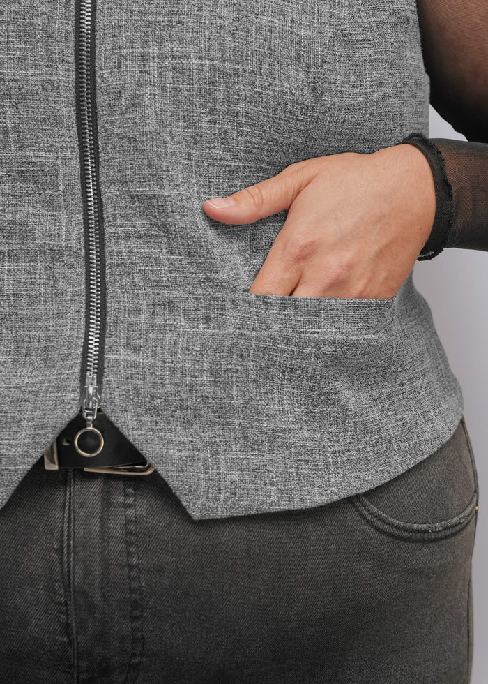 1X=Close-up of a person wearing a gray zip-front vest with a side pocket and hand inserted into the pocket, paired with dark gray jeans.