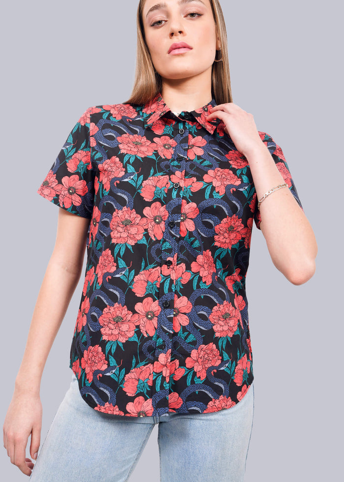 S= A woman wears The Essential Button Up by Wildfang, featuring a bold red, blue, and green floral pattern on breathable cotton, paired with light blue jeans as she poses against a plain white background.