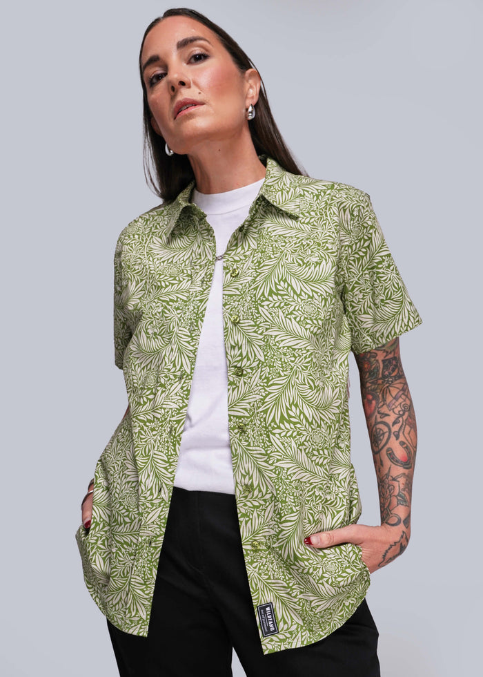 S=Person wearing a green patterned shirt over a white top with black pants on a plain background