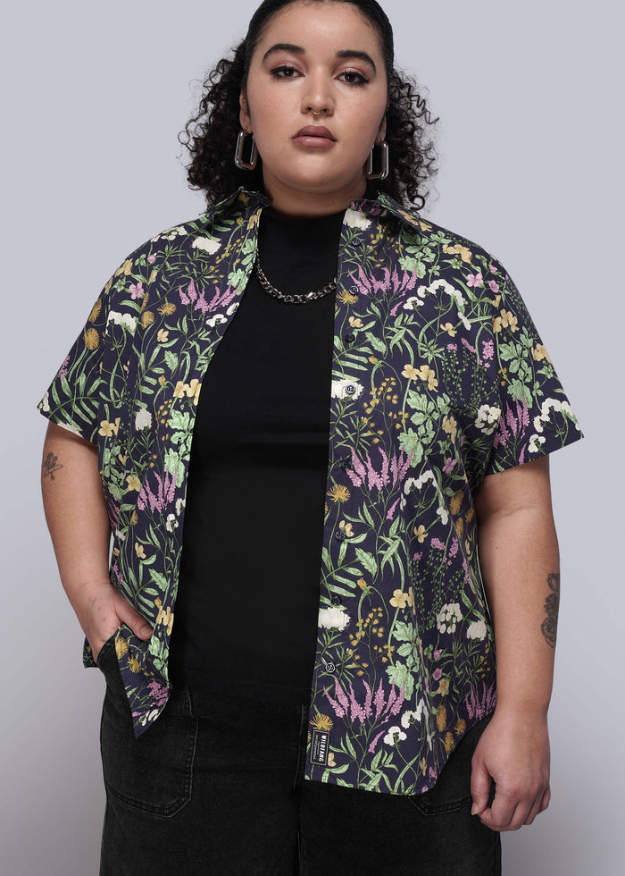 1X=Person wearing a colorful floral button up unbuttoned over a black top on a plain background