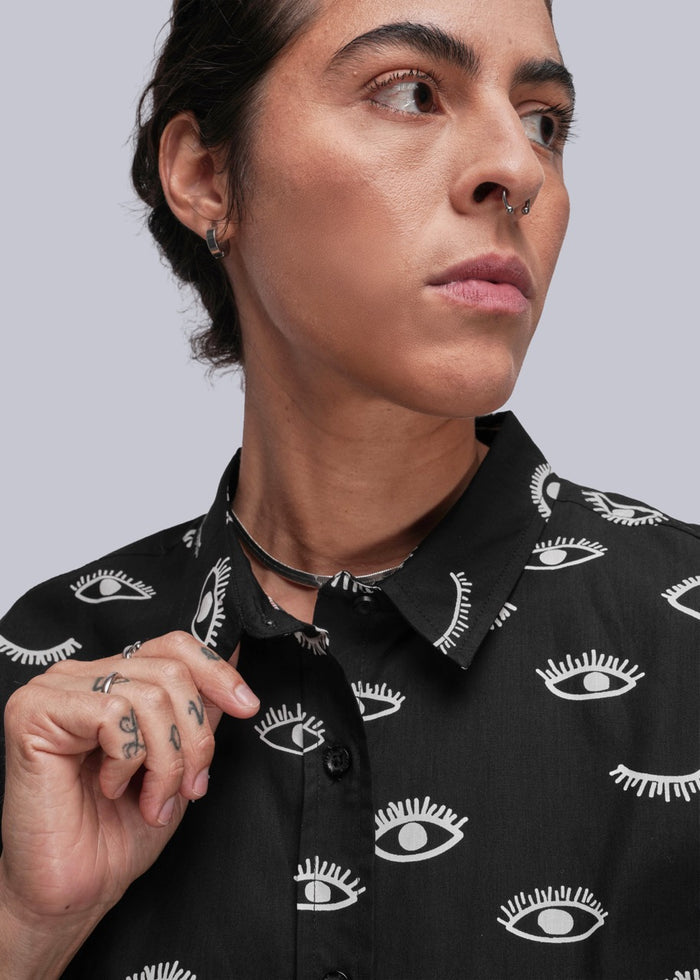 S=Person wearing a black shirt with white eye pattern against a gray background