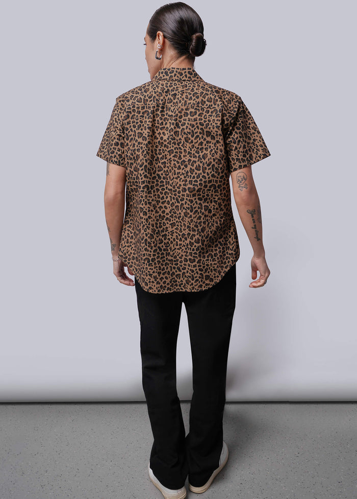 S=Person wearing a leopard print shirt and black pants against a plain background