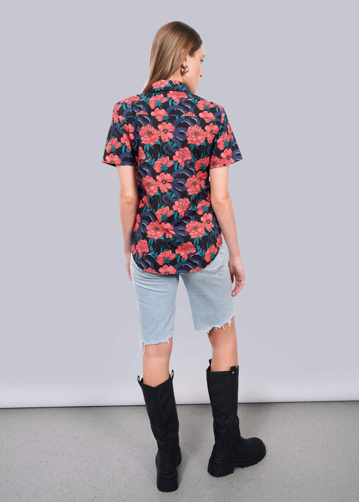 S= A woman stands facing away, wearing The Essential Button Up in tailored navy with a red floral pattern, light denim knee-length shorts, and black knee-high boots. She stands on a gray floor against a plain white wall.