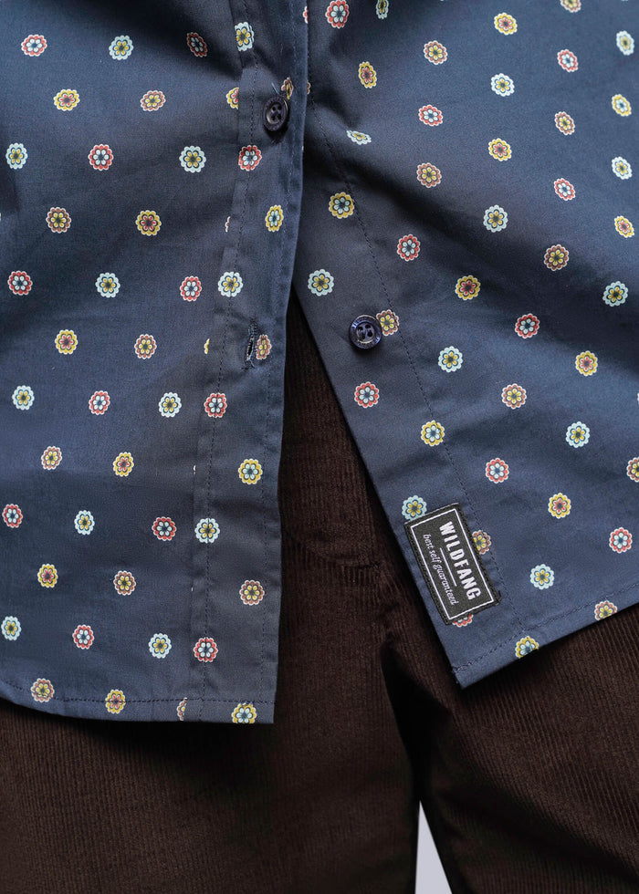 S=Close-up of a navy blue button-up shirt with a small multicolor geometric pattern, worn over dark brown corduroy trousers. A black brand label reading 'Mikrofashion' is visible near the hem.