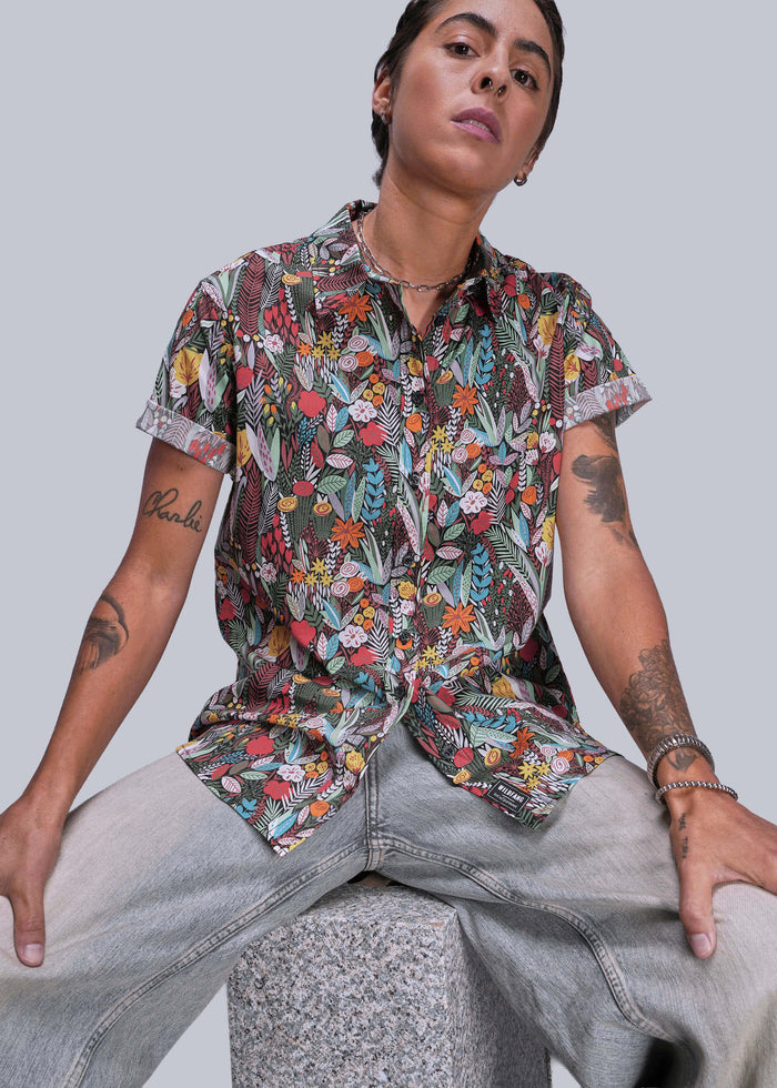 S=Person wearing a colorful floral shirt and light jeans against a plain background