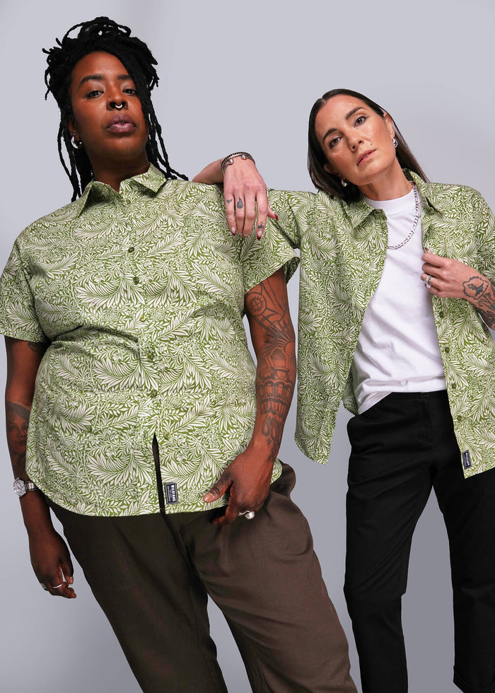 Two people wearing matching green patterned shirts against a gray background