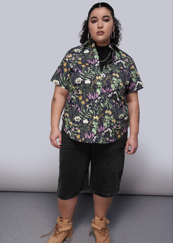 1X=Person wearing a floral shirt, black shorts, and brown boots on a plain background