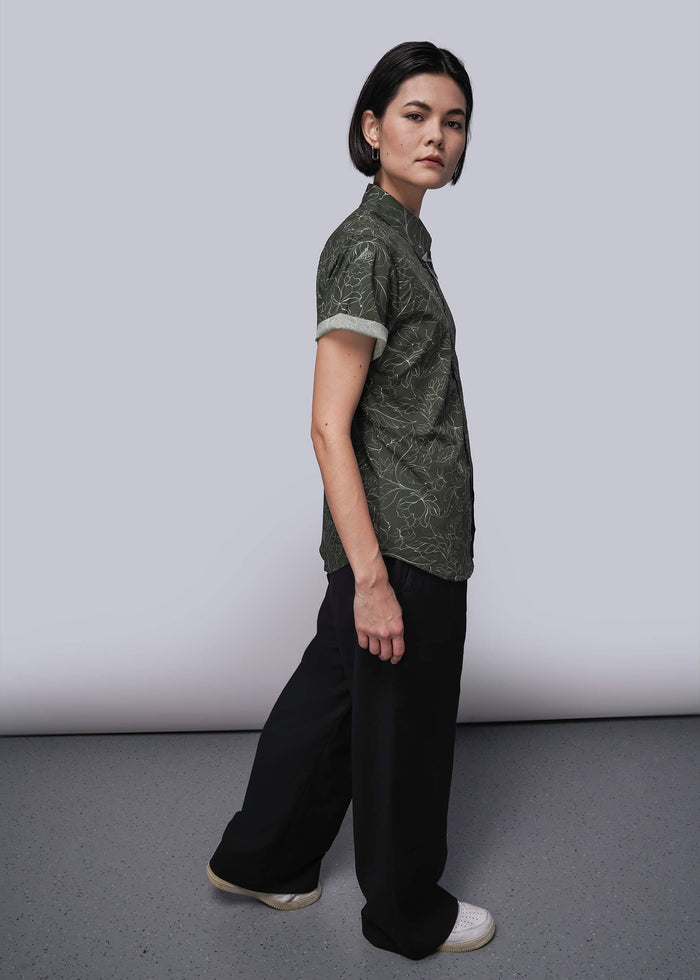 S=Person wearing a green patterned shirt and black pants against a white background