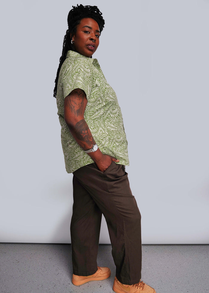 1X=Person wearing a green patterned shirt and brown pants against a plain background