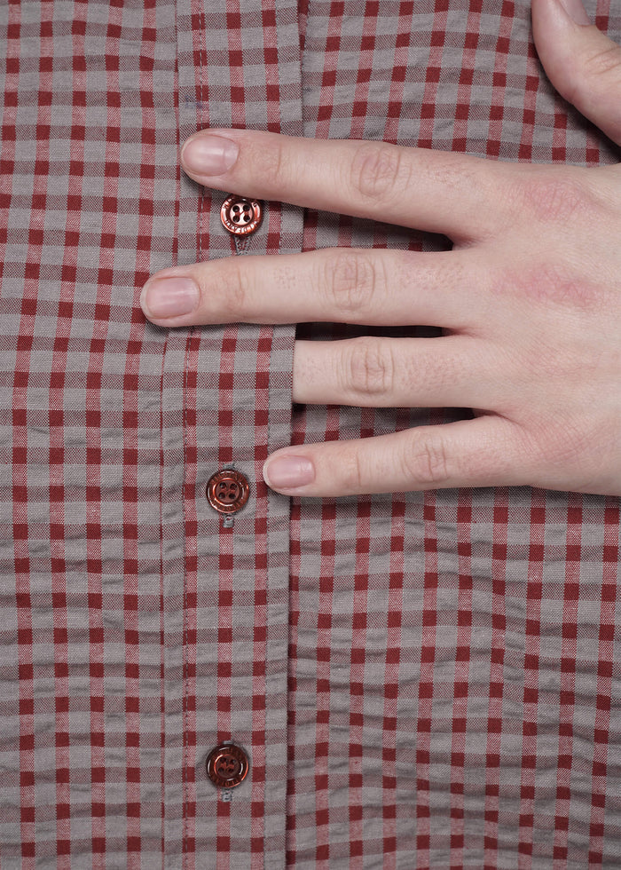 S=Hand pressing on a red and gray checkered shirt with visible buttons.
