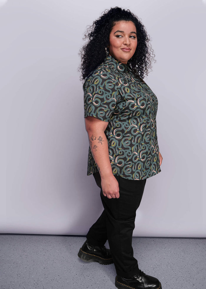 1X=Woman wearing a patterned shirt and black pants against a white background