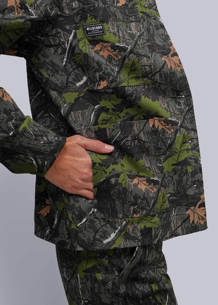 S=Close-up of a person wearing a camouflage jacket with a visible chest pocket and a small black brand patch reading WILDFANG, against a light gray studio background.