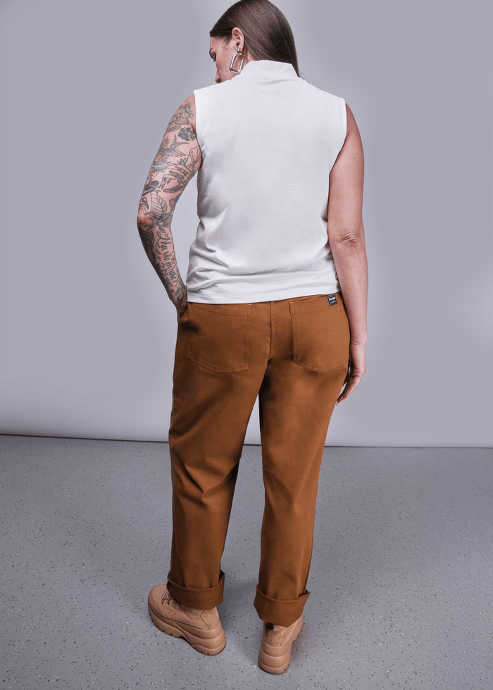 S=Back view of model with long brown hair standing in front of light grey background wearing The Everyday Mock Neck Tank in White and The Essential Utility Pant in Walnut with hand in pocket.