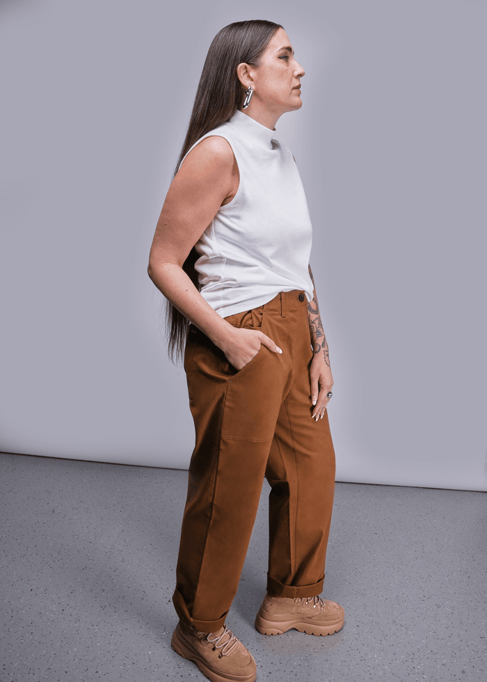 S=Side view of model with long brown hair standing in front of light grey background wearing The Everyday Mock Neck Tank in White and The Essential Utility Pant in Walnut with hand in pocket.
