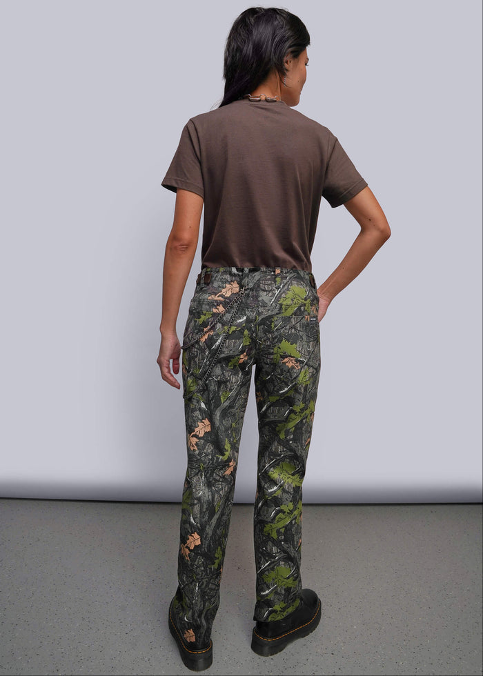 S=A model shown from the back wearing camouflage pants, a brown t-shirt, and black shoes against a plain gray studio background.
