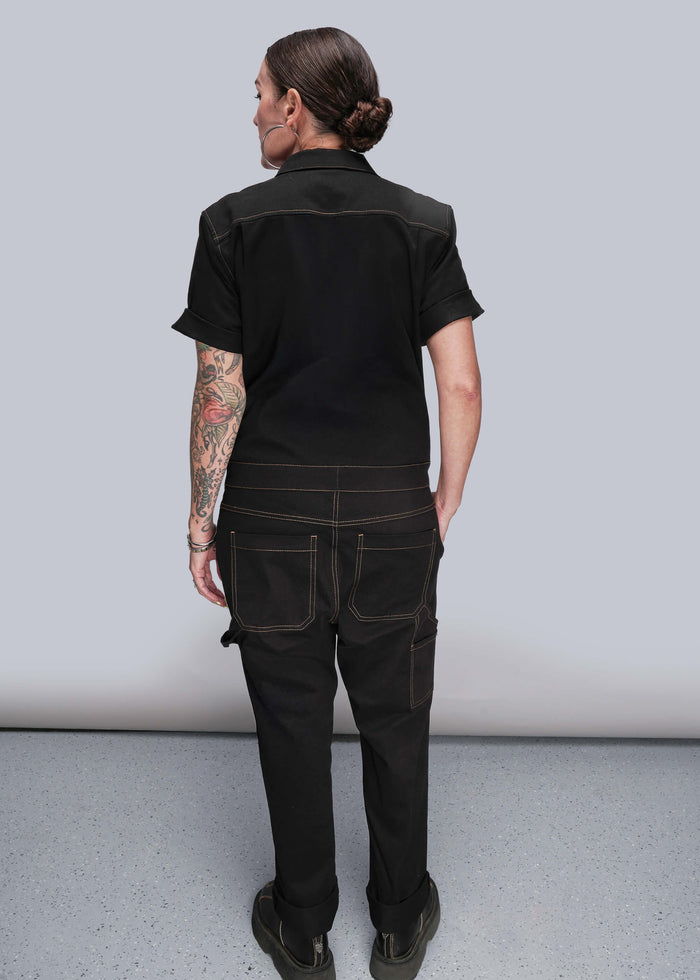 S=Person wearing a black jumpsuit against a plain background