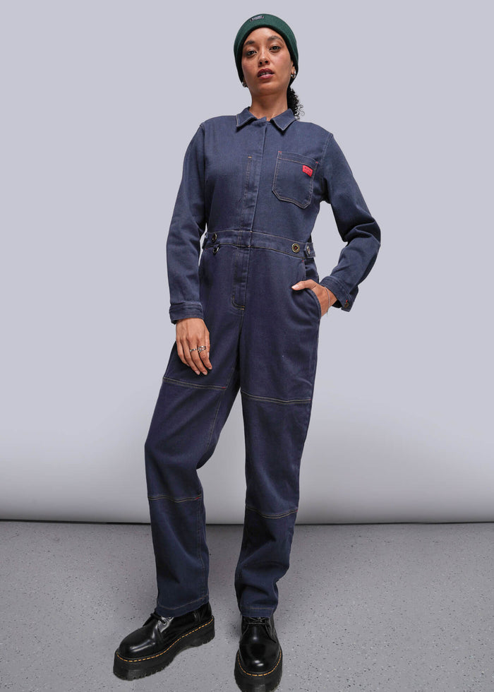 S=Person wearing a navy blue jumpsuit with a red pocket patch on a plain background