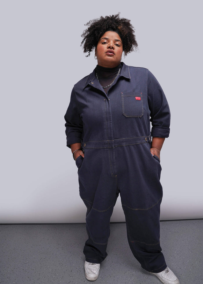1X=Person wearing a navy blue jumpsuit with a red label against a plain background