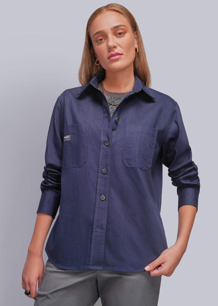 S=A woman modeling a navy blue long-sleeve button-up shirt with chest pockets, paired with gray pants, against a solid gray studio background.