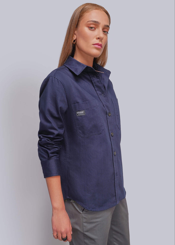 S=A woman modeling a navy blue long-sleeve button-up shirt with a chest pocket, paired with gray trousers, against a solid light gray background.
