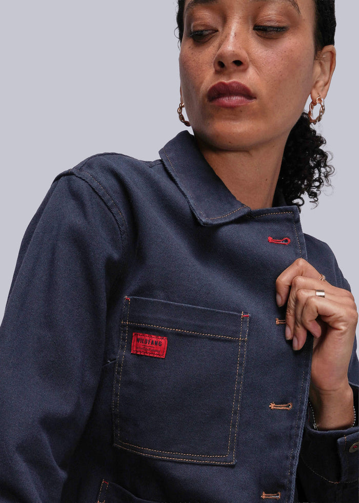 S=Person wearing a navy blue jean jacket with a red patch on a gray background