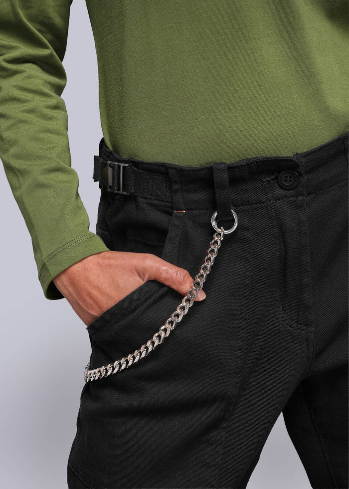 S=Person wearing a green shirt and black pants with a chain detail, standing against a plain background.