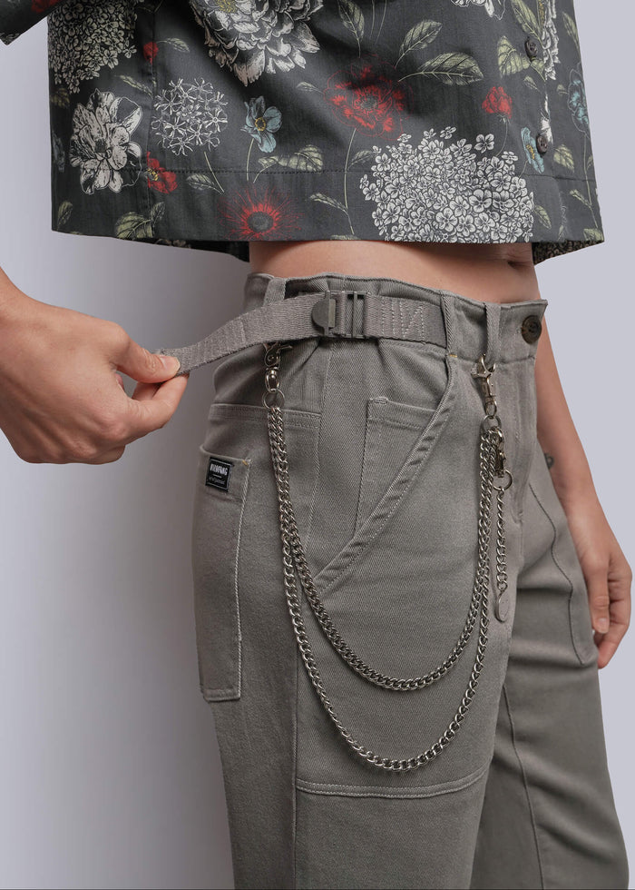 S=Close-up of a person wearing high-waisted gray cargo-style pants with a matching belt and hanging metal chain detail, paired with a cropped floral top against a light gray studio background.