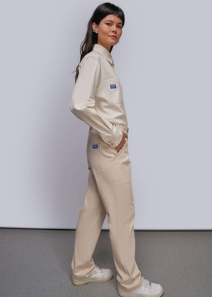 S=A woman modeling a light beige denim matching button up and utility pant paired with white sneakers, set against a plain light gray studio background.