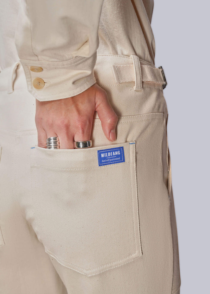 Close-up of a person wearing cream-colored denim matching shirt and pants, showing the back pocket with a blue 'WILDFANG' label and a hand resting in the pocket.