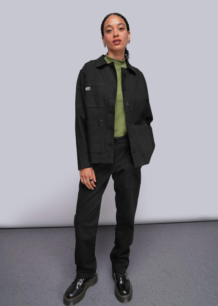 S=Person wearing a black jacket and pants with a green shirt underneath against a plain background
