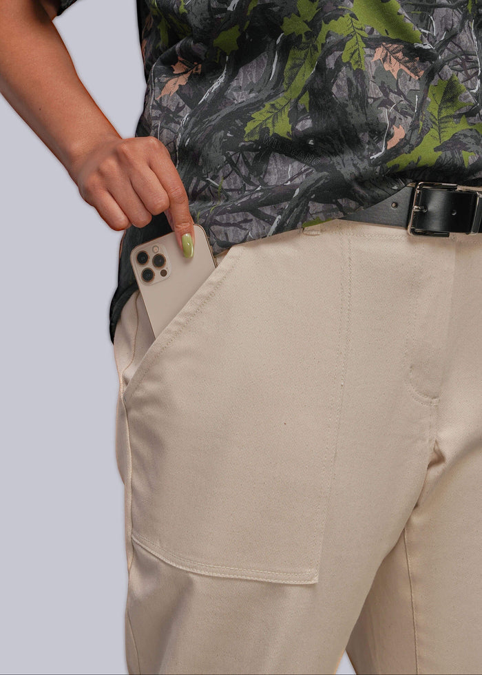 1X=A close-up of a person wearing beige cargo-style pants with a side pocket holding a smartphone, paired with a black belt and a dark camouflage shirt, against a light gray studio background.