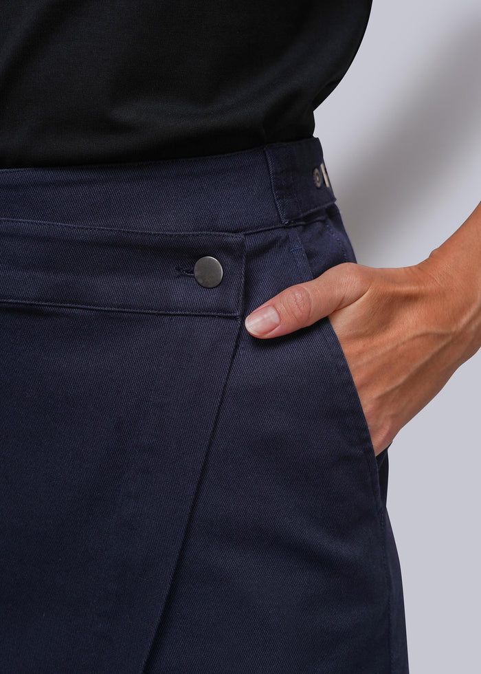 S=Close-up of a person wearing dark navy wrap skirt, showing the waistband, button closure, side pocket, and hand in the pocket. A black top is also visible at the top edge.