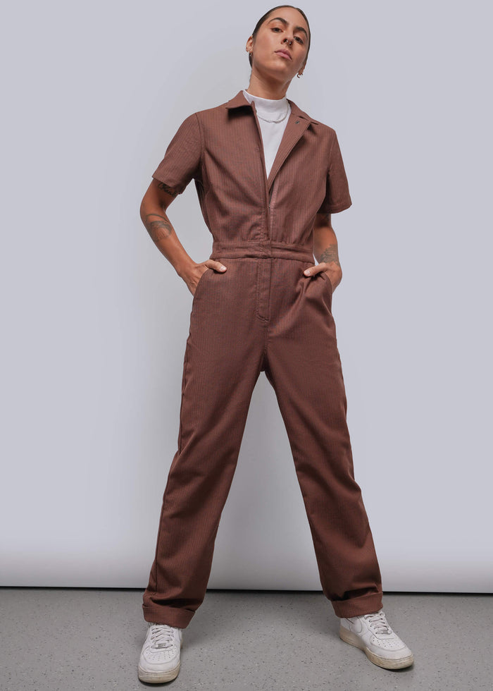 S=A model wearing a short-sleeve brown coverall with a zip-up front, standing against a light gray studio background.