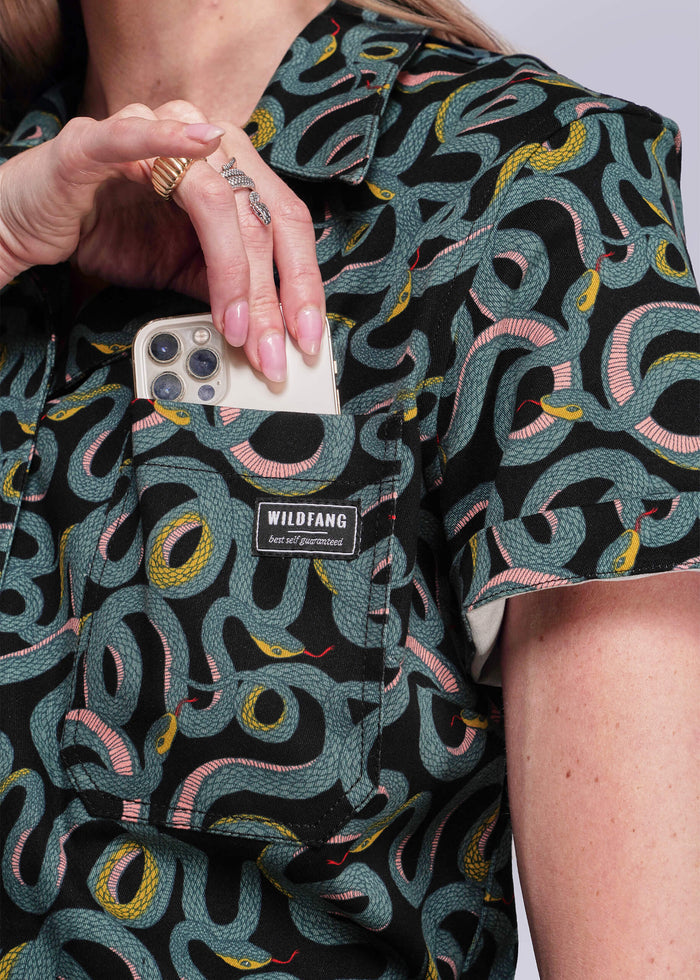S=Person wearing a patterned shirt with a visible brand label, holding a phone.