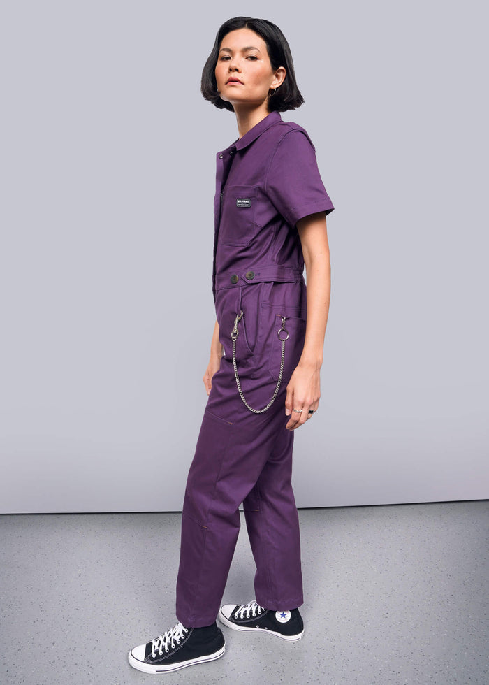 S=Person wearing a purple jumpsuit with black shoes on a gray background