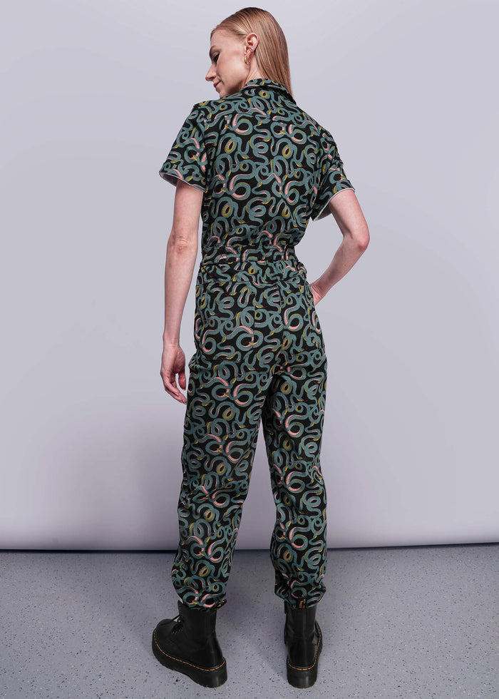 S=Person wearing a green patterned jumpsuit on a plain background