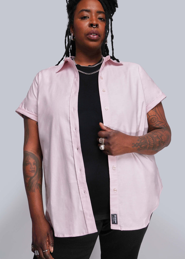 1X=Person wearing a light pink short-sleeve shirt over a black top against a gray background